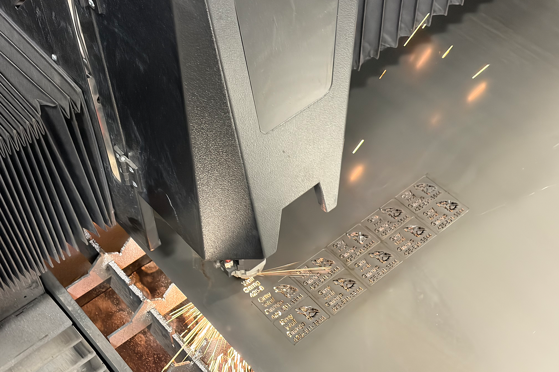 CNC laser head from above cutting etched metal tags with sparks